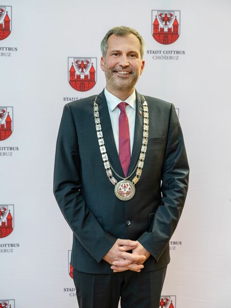 Ein Kind in einer gelben Warnweste steht an einer Straße und hält ein rotes Verkehrsschild.